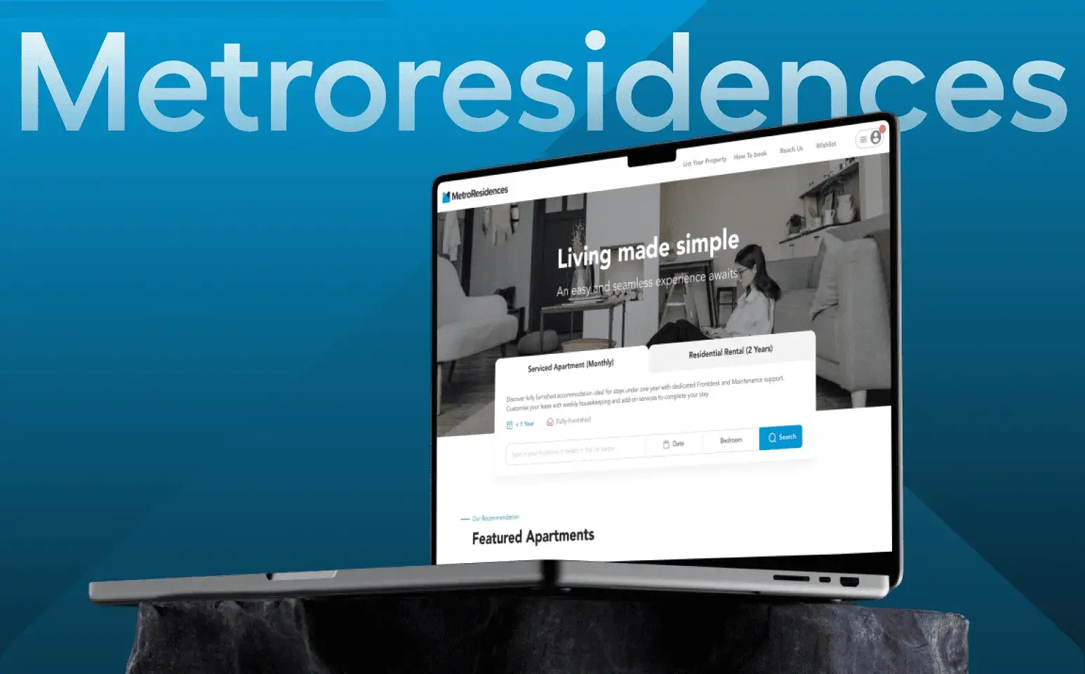 A laptop displaying the MetroResidences website is placed on a dark surface. The screen shows a homepage with the headline Living made simple and search options. The background features a large Metroresidences text.